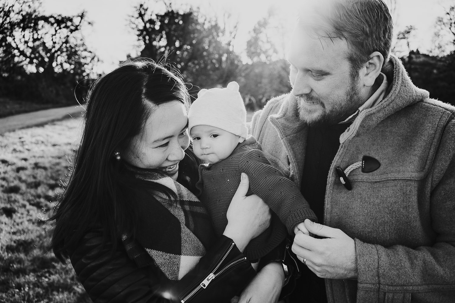 autumn mini photo shoot black and white photo of parents with toddler embracing in the park