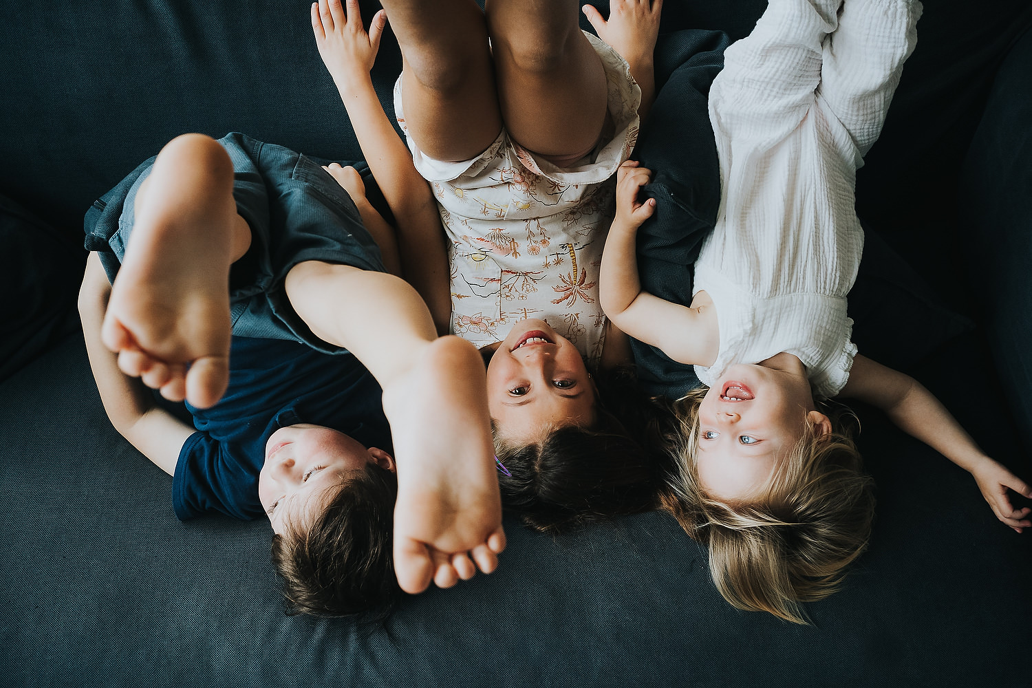 at home family photo shoots in london three siblings upside down on sofa