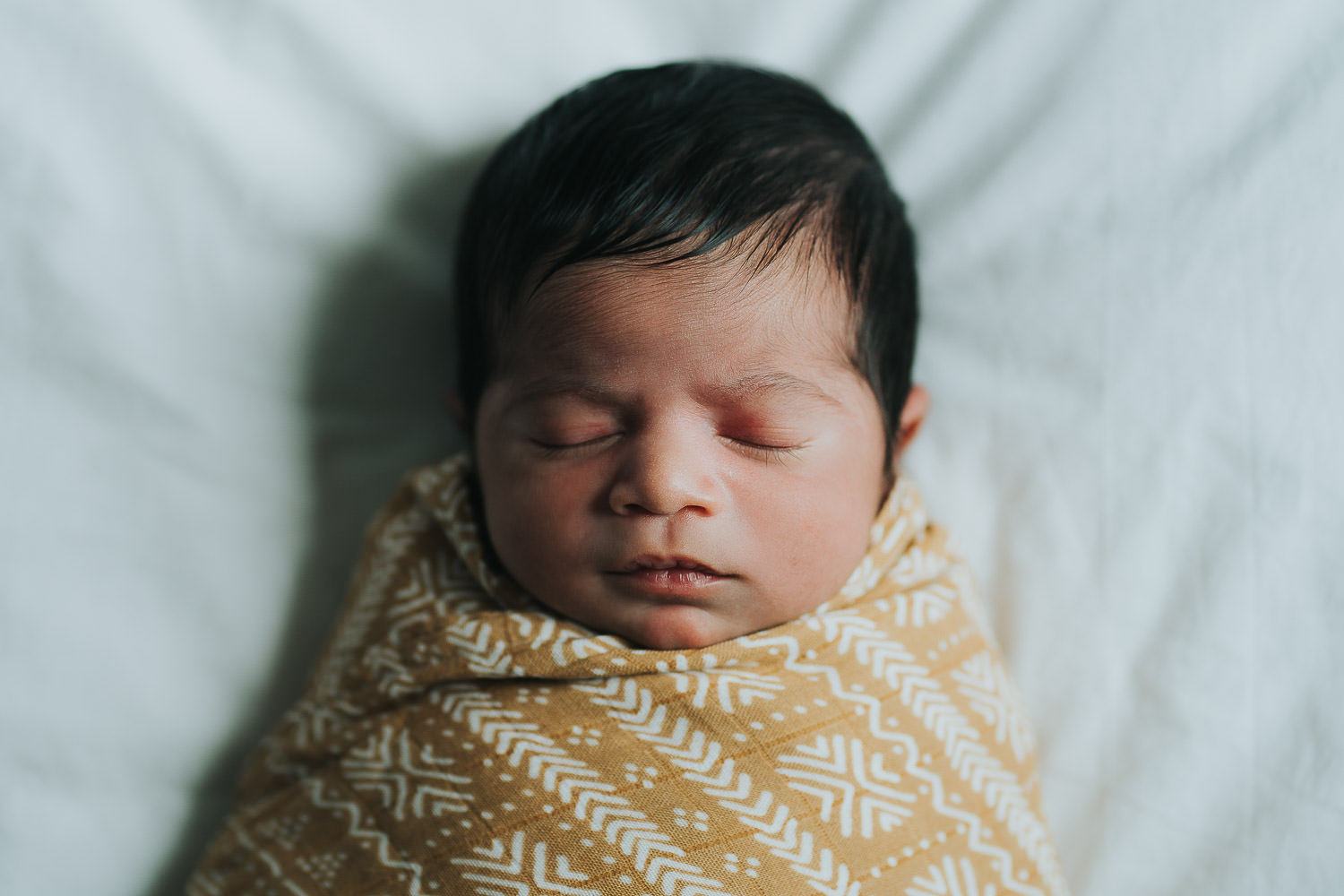 newborn photo shoot swaddled sleeping baby of colour on bed