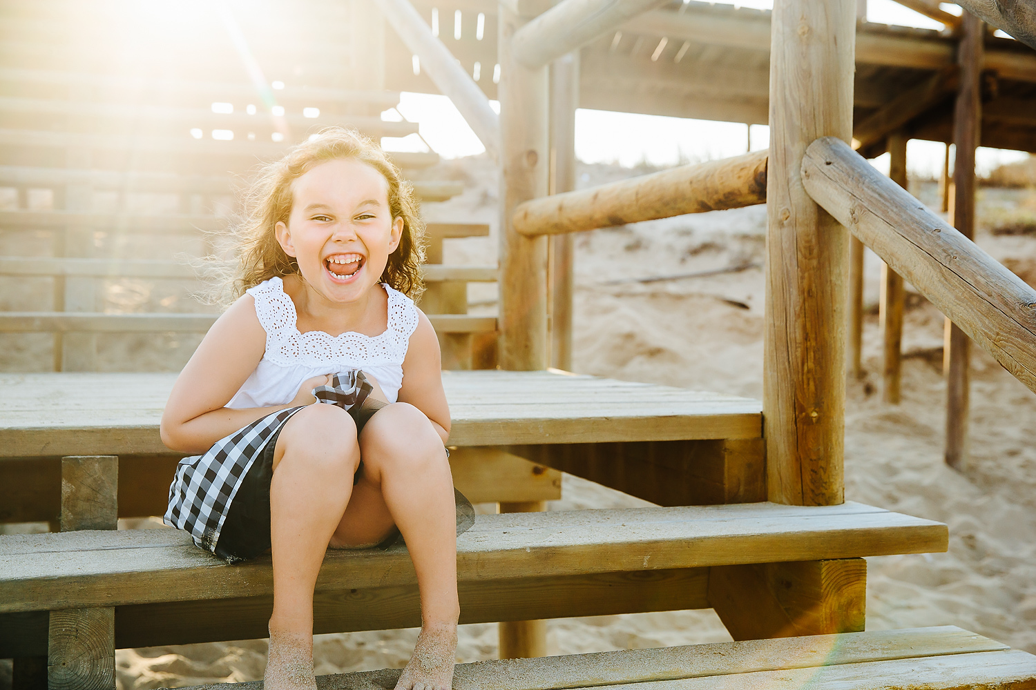 FAMILY VACATION PHOTO SHOOTS GIRL SITTING ON WOODEN BEACH STEPS LAUGHING